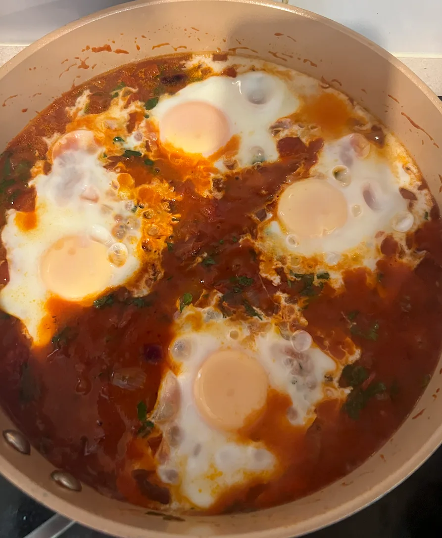 Four eggs poaching in a pan of spiced tomato sauce.